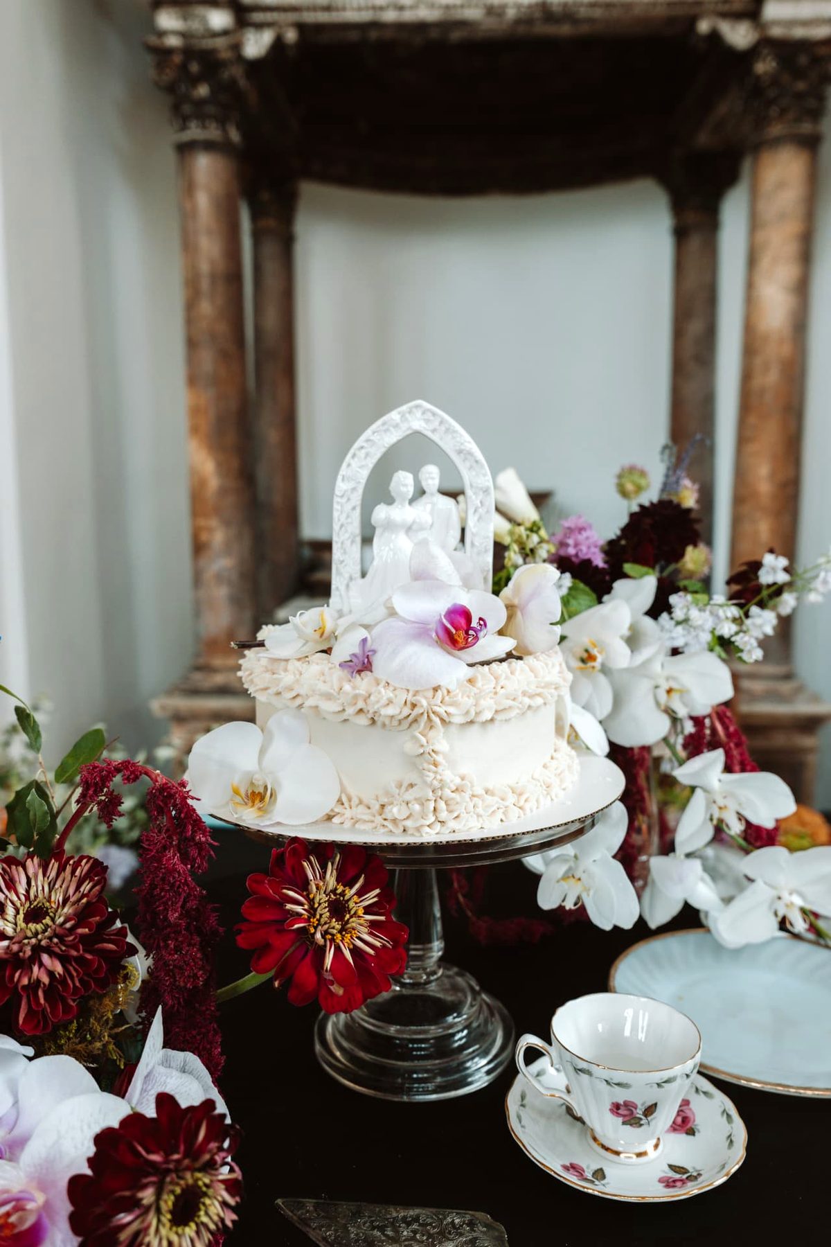 Vintage ivory wedding cake with orchids, antique topper, and a floral teacup
