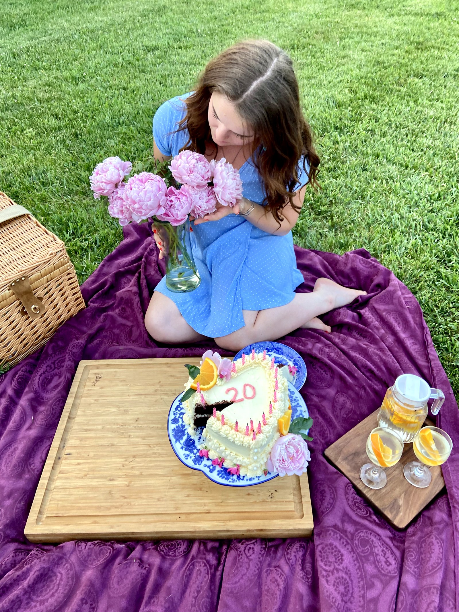 A birthday picnic on a purple blanket with a heart cake, peonies, and sunshine