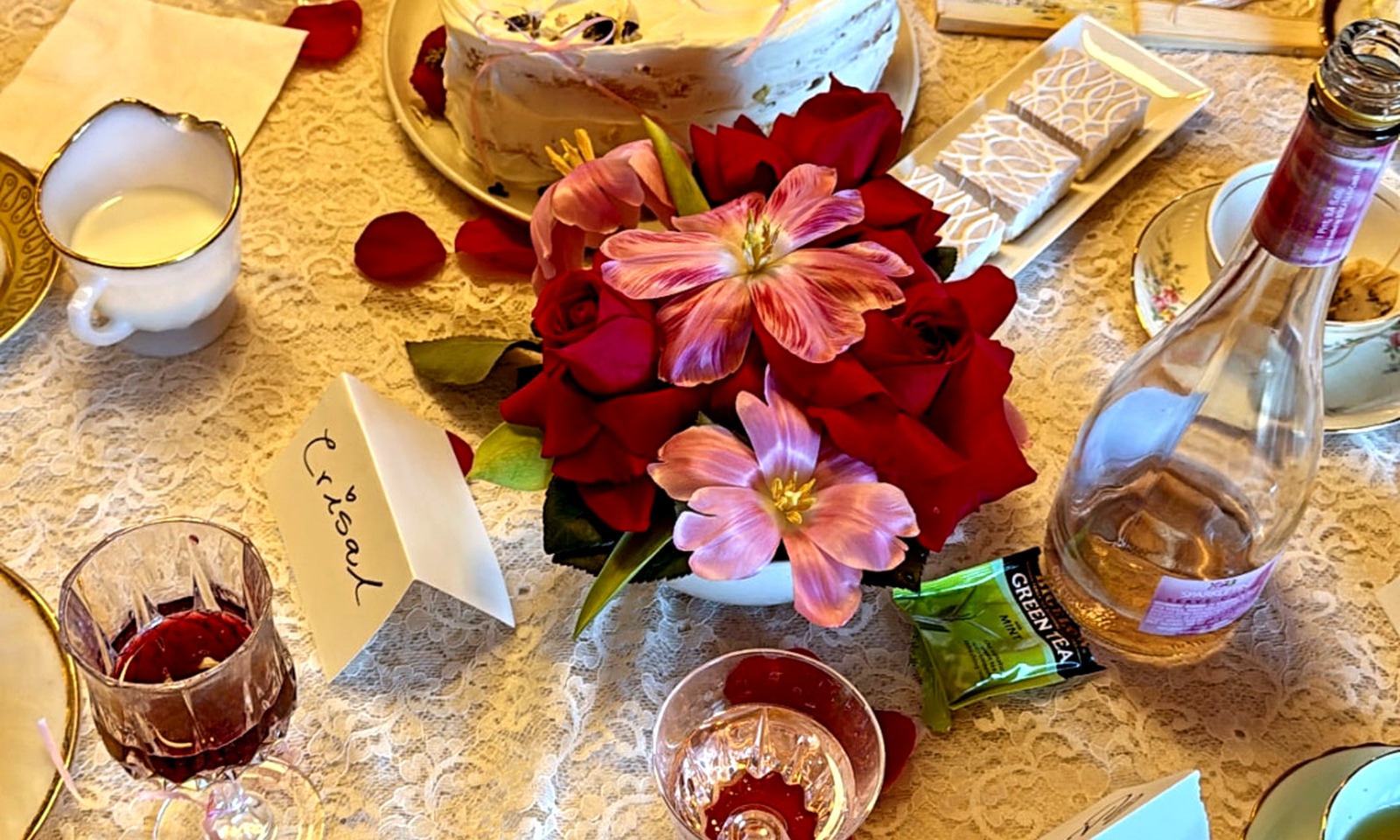 A tea-party table set with a heart-shaped cake, roses, candles, and fine china