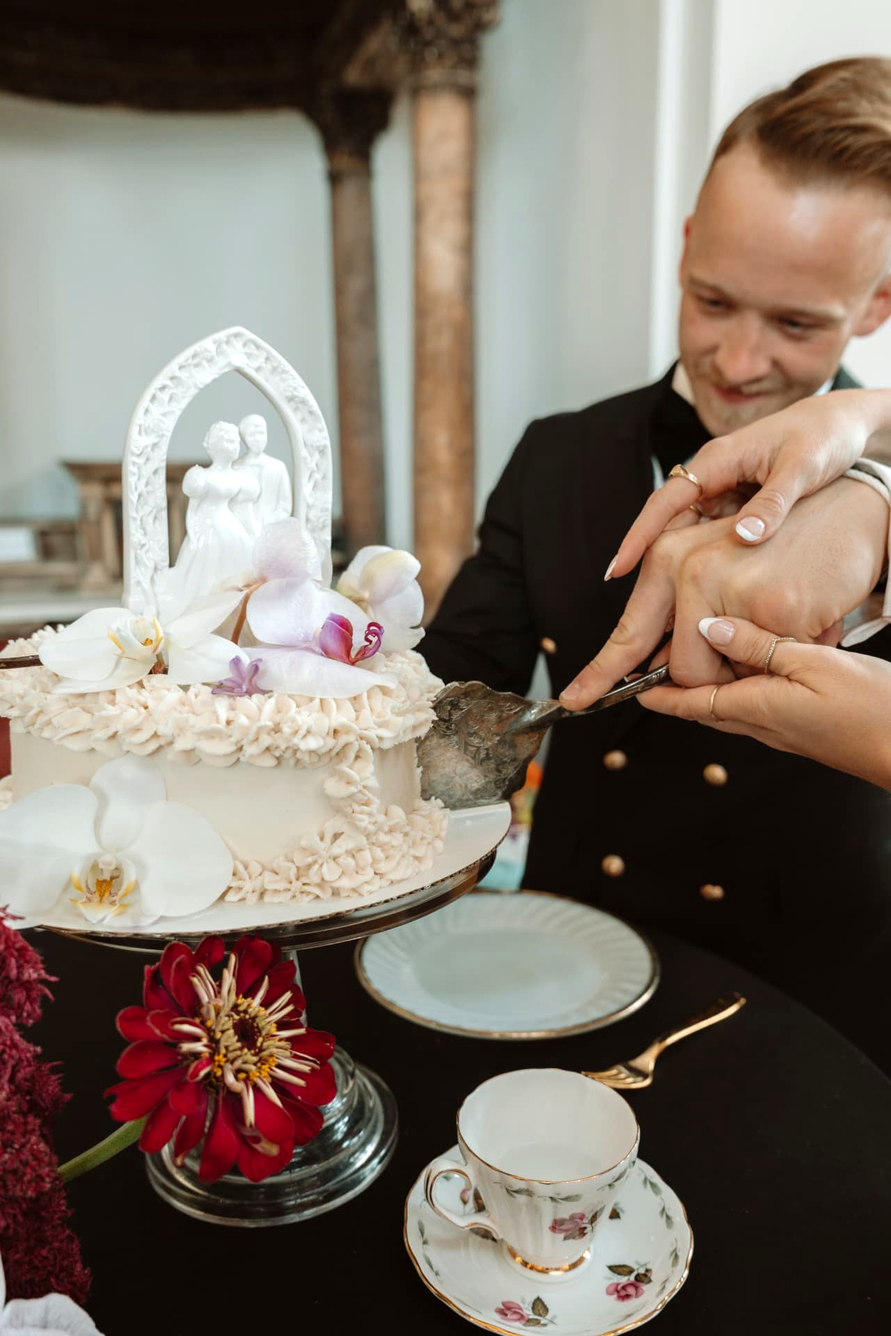 A couple cutting their vintage orchid wedding cake with an antique topper